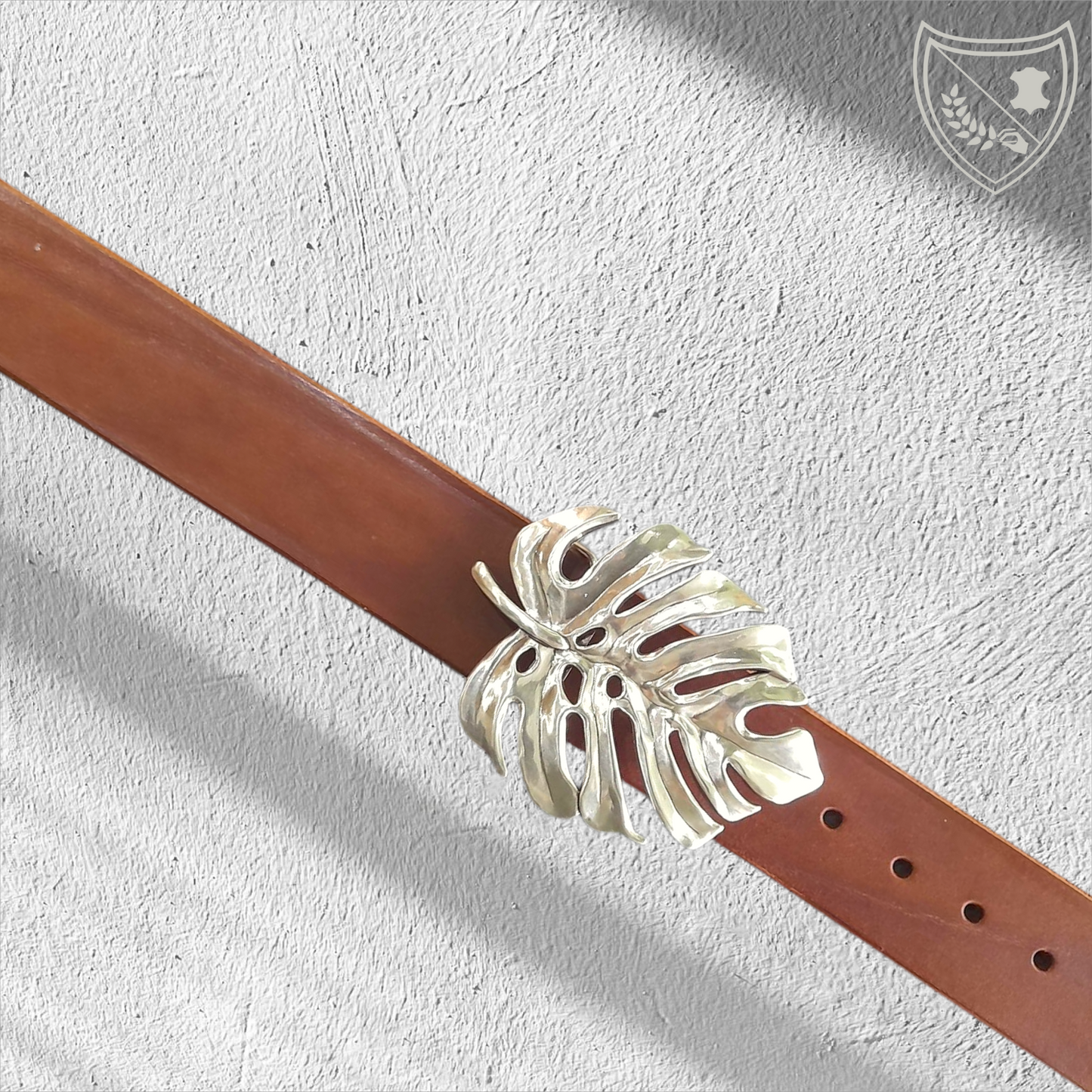Ceinture cuir végétal de couleur havana avec boucle de ceinture Monstera en métal argenté, feuille ajourée au design organique, élégante et affirmée, fermoir fiable pour confort et maintien.