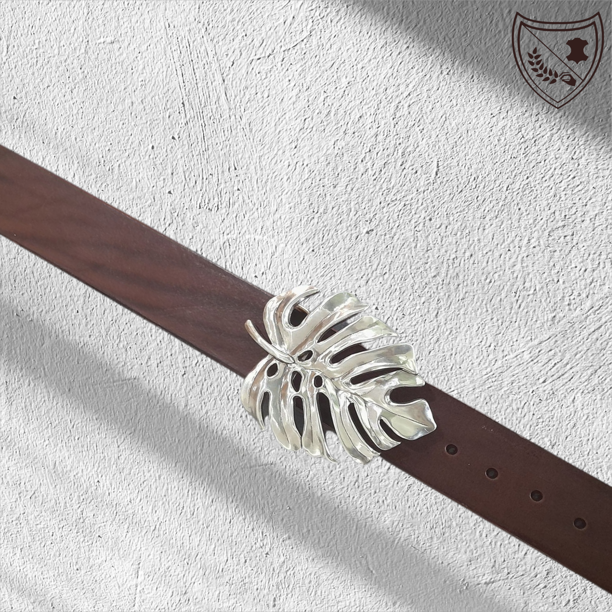 Ceinture cuir végétal de couleur chocolat avec boucle de ceinture Monstera en métal argenté, feuille ajourée au design organique, élégante et affirmée, fermoir fiable pour confort et maintien.